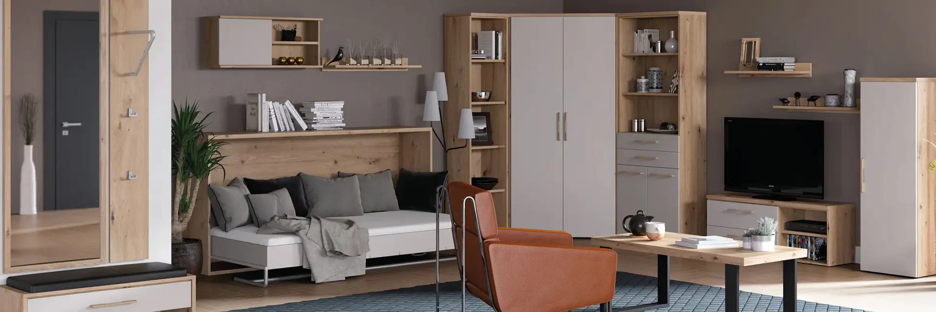 Komplette Wohnwand in Holz und Weiss mit Sofa, Eckschrank, Hängeregalen und TV-Board, vorn Couchtisch und cognacfarbenem Sessel auf blauem Teppich.